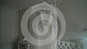 Luxury wedding dress hanging in bedroom. Silhouette of amazing bride`s lace gown in light. Morning preparation, getting