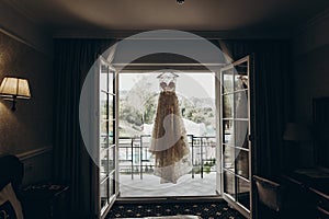 Luxury wedding dress hanging on window in a hotel room. silhouet