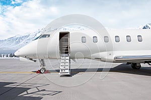 Luxury white corporate aircraft with an opened gangway door at winter on the background of high snow capped mountains