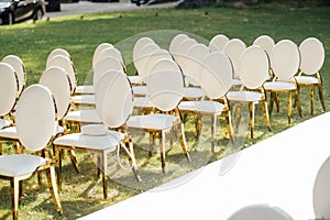 Luxury white-golden chairs on wedding ceremony outdoors. Festive decorations. Empty rows armchairs for guests.