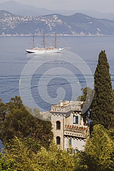 Luxury white sailboat in Portofino with sea, mountains, cliffs and villas.