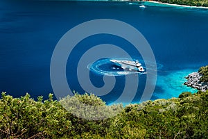 Luxury white yacht sail boat anchoring in a tranquil bay in deep blue water water, near picturesque shore of greek