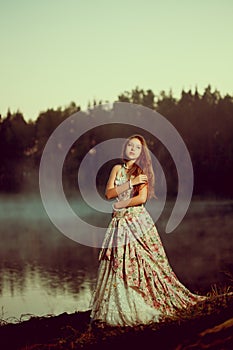 Luxury woman in a forest in a long vintage dress near the lake.