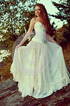 Luxury woman in a forest in a long vintage dress near the lake.