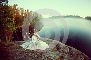 Luxury woman in a forest in a long vintage dress near the lake.