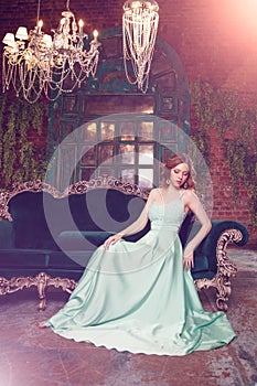 Luxury woman model in a mint-colored dress sitting on a vintage couch. Beauty girl with a stunning makeup and hairstyle