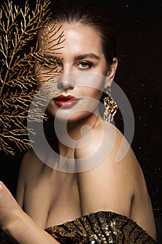 Luxury Woman Portrait with Gold Jewelry. Mystery Girl hiding Face. Glitter Make up. Elegant Lady over Black Background