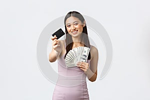 Luxury women, party and holidays concept. Gorgeous asian woman in stylish dress, holding money and giving credit card
