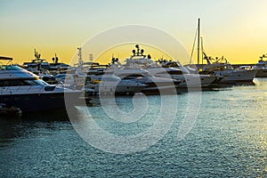 Luxury yachts docked in sea port at sunset. Marine parking of modern motor boats and blue water. Tranquility, relaxation