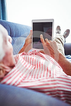 Lying on a couch senior man touching digital tablet