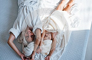 Lying down on bed. Young mother with her daugher have beauty day indoors in white room