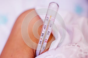 Lying sick woman with thermometer in the armpit . Woman measures body temperature under his arm with digital thermometer