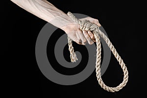 Lynching and suicide theme: man's hand holding a loop of rope for hanging on black isolated background