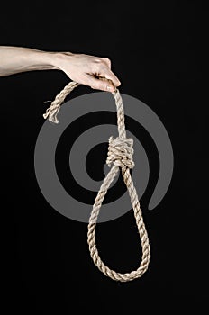 Lynching and suicide theme: man's hand holding a loop of rope for hanging on black isolated background