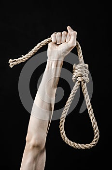Lynching and suicide theme: man's hand holding a loop of rope for hanging on black isolated background