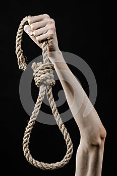 Lynching and suicide theme: man's hand holding a loop of rope for hanging on black isolated background