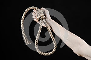 Lynching and suicide theme: man's hand holding a loop of rope for hanging on black isolated background