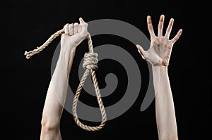 Lynching and suicide theme: man's hand holding a loop of rope for hanging on black isolated background