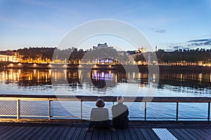 Senior people, and old couple of lovers, sitting on the quays of the riverbank of the rhone admiring the river during evening