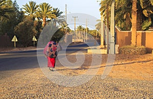 M'hamid, Morocco - February 22 2016: Woman carrying jute burlap sack during evening