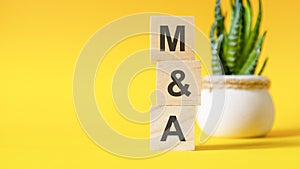 M and A - Mergers and Acquisitions - concept with wooden blocks on table, yellow background