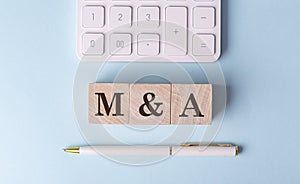 M and A on wooden cubes with pen and calculator, financial concept