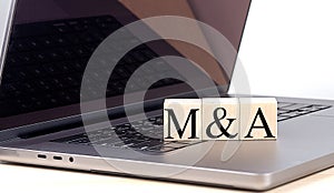 M and A word on wooden block on a laptop , business concept photo