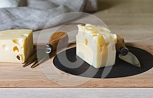 Maasdam cheese on a black stone cutting board with a cheese knife. Copy space