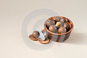 Macadamia nuts in ceramic bowl on beige background. Nuts with sawn nutshells and with opener key on the wooden spoon. Healthy