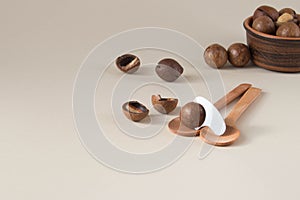 Macadamia nuts in ceramic bowl on beige background. Nuts with sawn nutshells and with opener key on the wooden spoon. Healthy