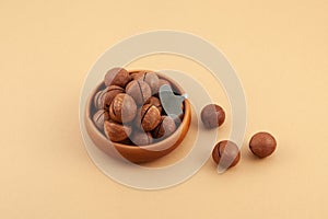 Macadamia nuts in clay bowl on beige background, top view. Macadamia is delicious nut with hardshell