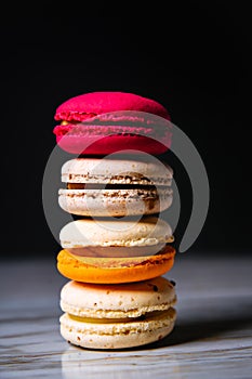 Macaron pink, orange and beige, blue on marble style and black background. French dessert on top of each other photo