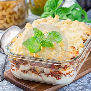 Macaroni casserole with ground beef, cheese and tomato in  glass baking dish, square format