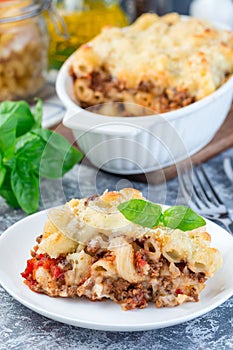 Macaroni casserole with ground beef, cheese and tomato on a white plate, vertical