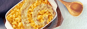 Macaroni and cheese pasta in a casserole panorama, top shot with a wooden spoon