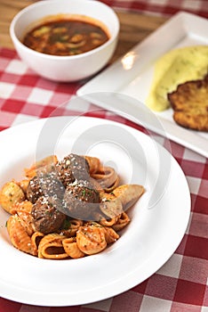 Macaroni dinner with meatballs. Meat pasta served in a white plate over red plaid tablecloth