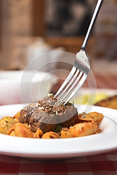 Macaroni dinner with meatballs. Meat pasta served in a white plate over red plaid tablecloth