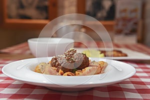 Macaroni dinner with meatballs. Meat pasta served in a white plate over red plaid tablecloth