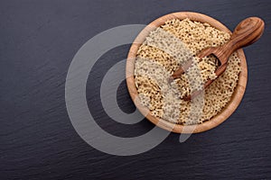 Macaroni in the form of starlets lie in a wooden cup and a wooden scoop on a black stone board, space for text