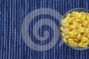Macaroni ruote Pasta in a glass cup on a striped white blue cloth background with a side. Close-up with the top. Free