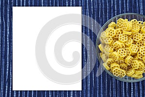 Macaroni ruote Pasta in a glass cup on a striped white blue cloth background with a side. Close-up with the top. White