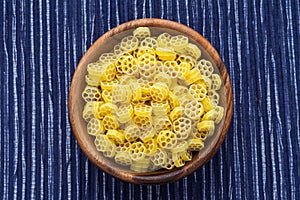 Macaroni ruote pasta in a wooden bowl on a striped white blue cloth background in the center. Close-up with the top.