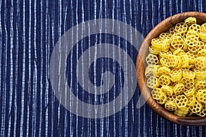 Macaroni ruote pasta in a wooden bowl on a striped white blue cloth background with a side. Close-up with the top. Free