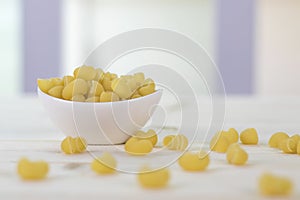 Macaroni are in a white cup placed on a wooden table.