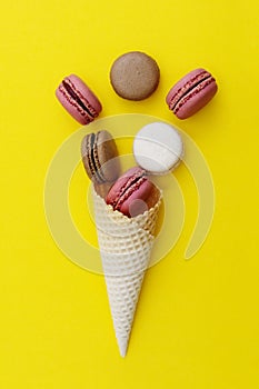 Macarons cakes. Stil life photo of waffle cone with macaroons on yellow background. Flat lay, dessert