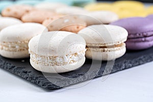 Macarons are laid out on a black slate in beautifully colored rows.