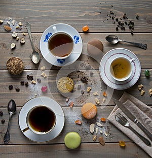 Macarons multicolored, cups with black and green tea and with coffee, vintage spoons, fork and knife on a wooden table with variou