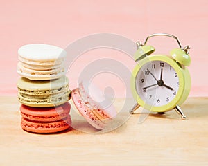 Macaroons and alarm clock on table, vintage stylized photo