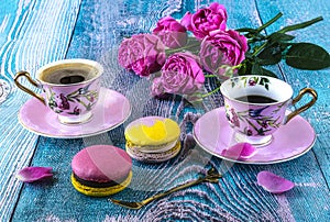 Macaroons and two pink cups of coffee and peony blooming pink roses