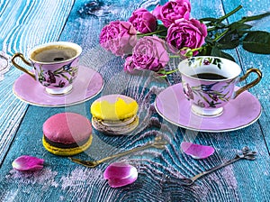 Macaroons and two pink cups of coffee and peony blooming pink roses